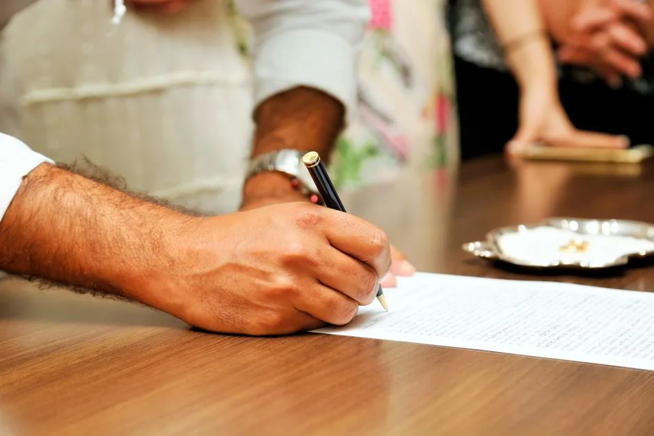 Personne en tenue professionnelle signant un document sur une table en bois dans un cadre de bureau.